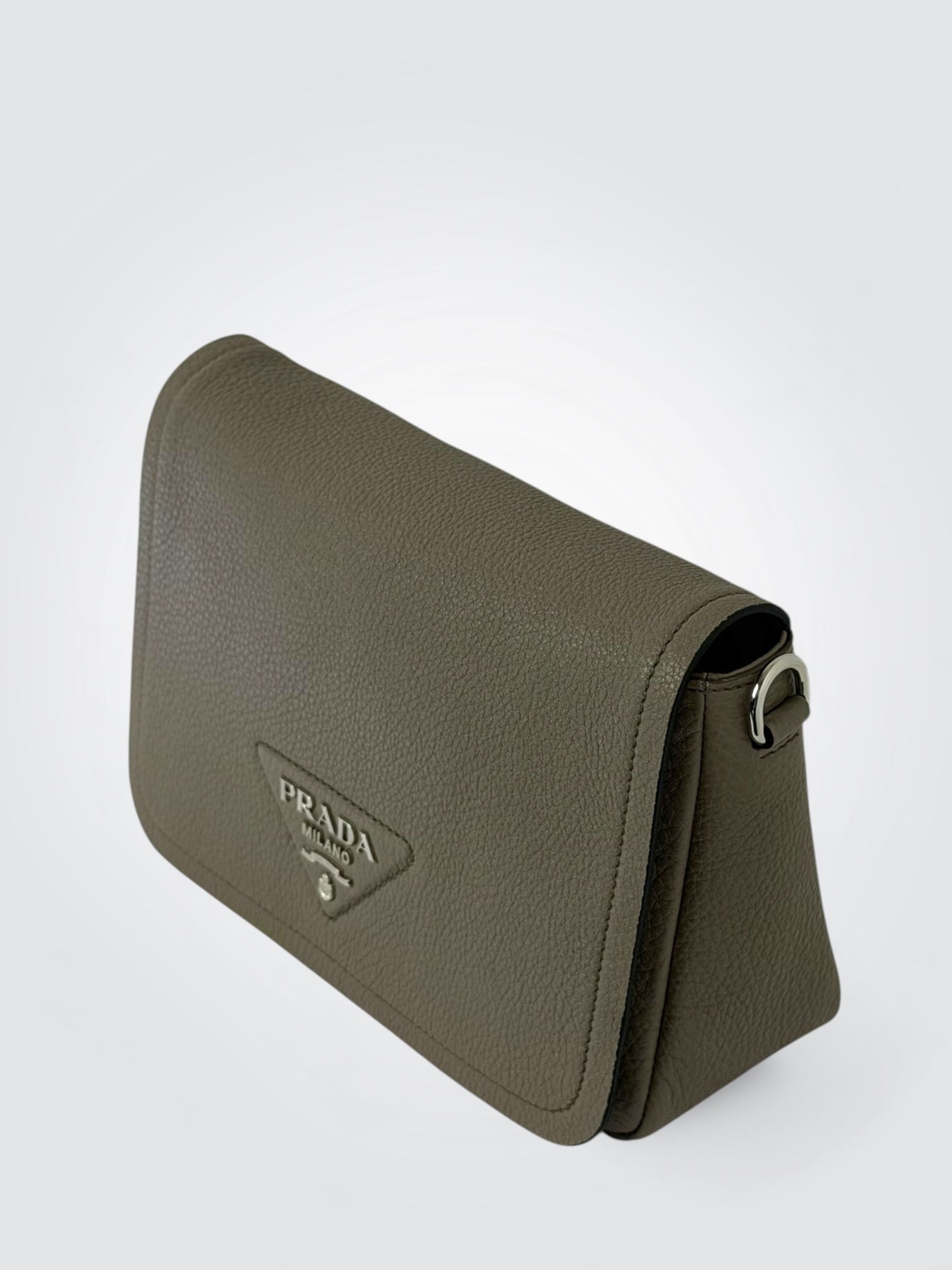 Prada Vitello Daino Soft Flap Crossbody in the argilla (clay grey) colorway, featuring textured calfskin leather and a logo-print embroidered woven strap