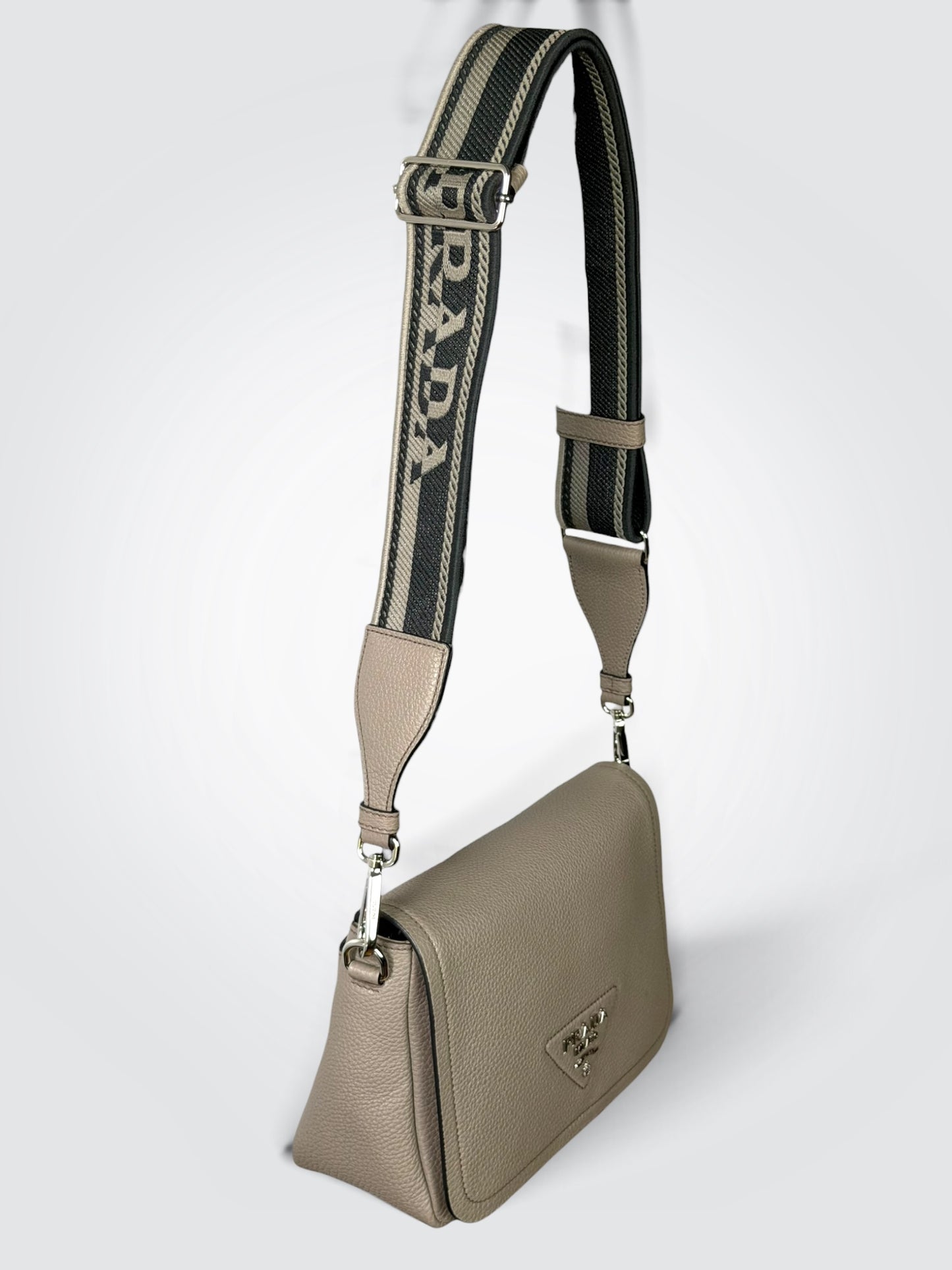 Prada Vitello Daino Soft Flap Crossbody in the argilla (clay grey) colorway, featuring textured calfskin leather and a logo-print embroidered woven strap