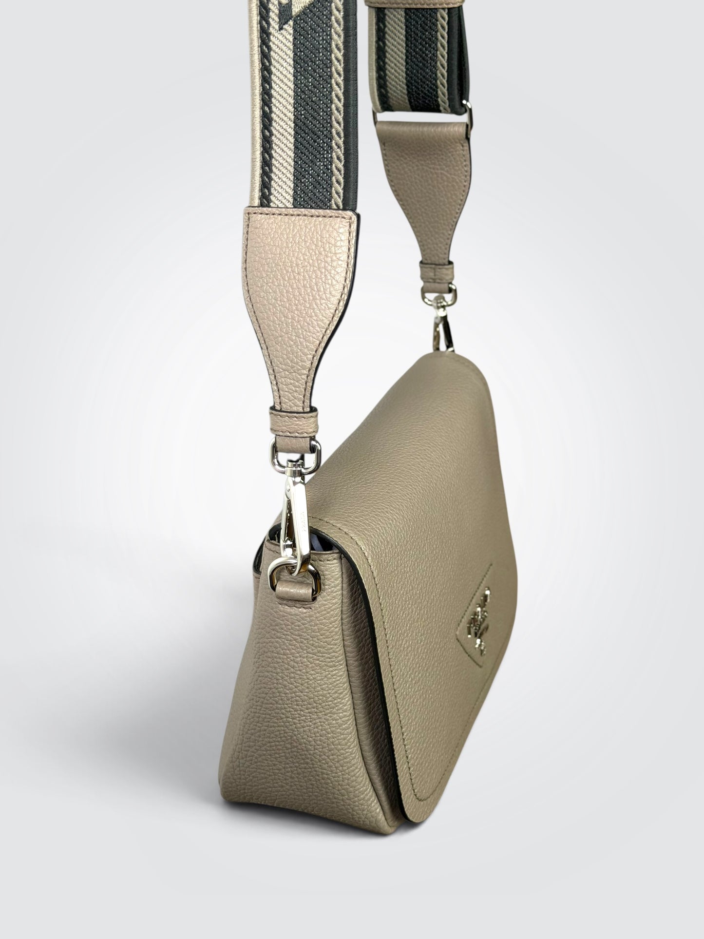 Prada Vitello Daino Soft Flap Crossbody in the argilla (clay grey) colorway, featuring textured calfskin leather and a logo-print embroidered woven strap