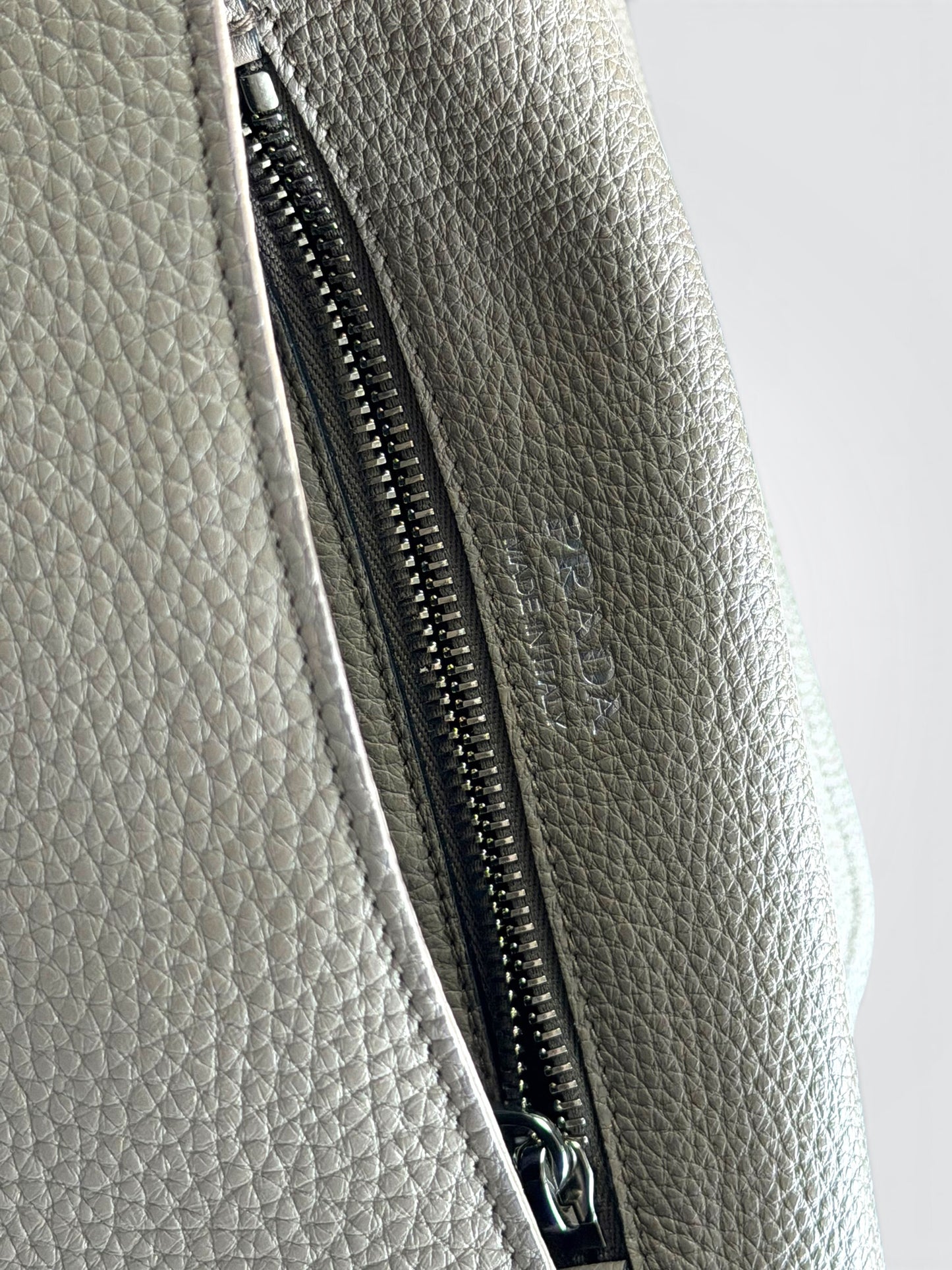 Prada Vitello Daino Soft Flap Crossbody in the argilla (clay grey) colorway, featuring textured calfskin leather and a logo-print embroidered woven strap